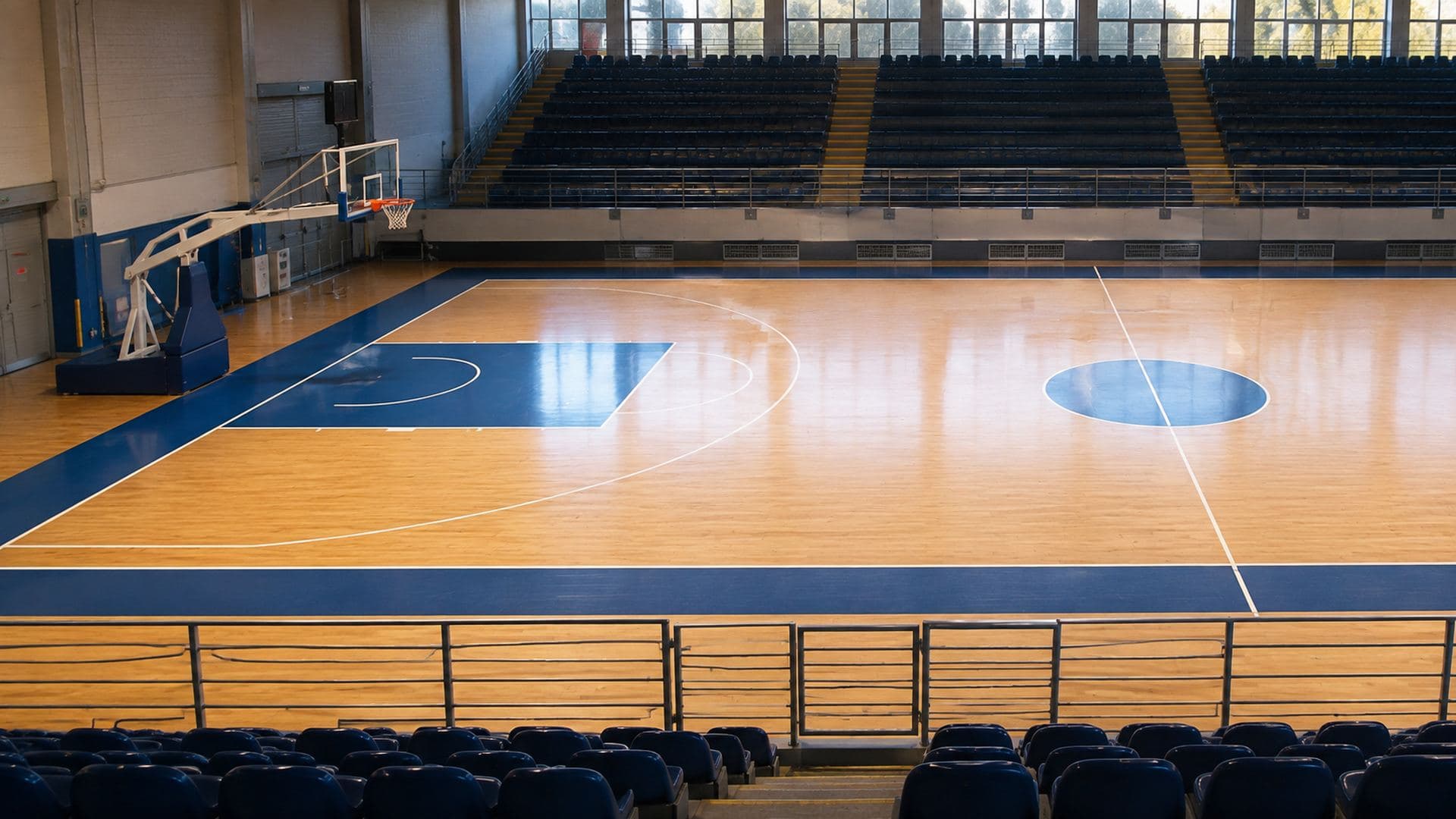 Campo da pallacanestro vuoto visto dalle tribune, con la linea da tre punti e l'area ben visibili